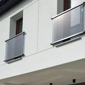 Französischer Balkon mit Glasgeländer an moderner Hausfassade aus weißem Putz.