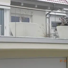 Moderne Dachterrasse mit Glasgeländer, großen Pflanzkübeln und winterlicher Bepflanzung.