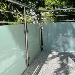Moderner Balkon mit satiniertem Glasgeländer und Edelstahlpfosten im Sonnenschein.