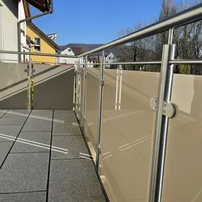 Moderner Balkon mit Edelstahlgeländer und Sichtschutz aus hellen Kunststoffplatten.