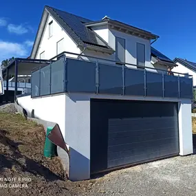 Modernes Einfamilienhaus mit Glasbalkon und großer Garage in Neubausiedlung.