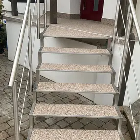 Außentreppe mit Edelstahlgeländer und Steintreppenstufen vor einem Hauseingang.