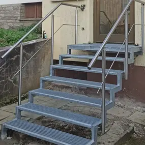 Metalltreppe mit modernem Edelstahlgeländer führt zum Hauseingang eines Einfamilienhauses.