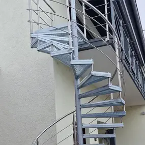 Metallwendeltreppe außen am Haus mit Geländer und verzinkten Stufen für Balkonzugang.