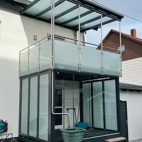 Moderner Balkon mit Glasüberdachung und Glasgeländer an einem Einfamilienhaus.