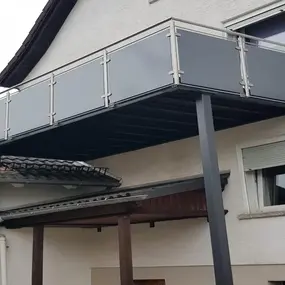 Moderner Balkon mit mattem Glasgeländer und Stahlträgern an einem Einfamilienhaus.