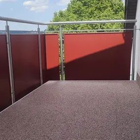Moderner Balkon mit rotem Sichtschutz, Edelstahlgeländer und neuem Bodenbelag.