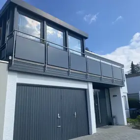 Modernes Einfamilienhaus mit großer Garage, Balkon und viel Glasfassade unter blauem Himmel.