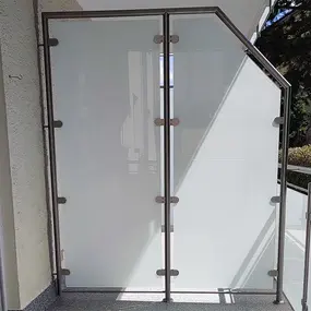 Balkon mit satiniertem Glas als Sichtschutz und Edelstahlrahmen bei Tageslicht.