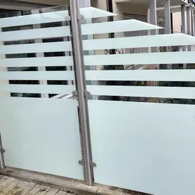Moderner Sichtschutzzaun aus satiniertem Glas mit Edelstahlpfosten vor Wohngebäude.