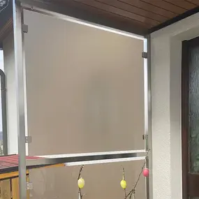 Sichtschutz aus Milchglas mit Metallrahmen auf einem Balkon neben einer Haustür montiert.