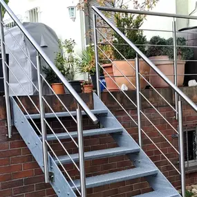 Außentreppe aus Metall mit Edelstahlgeländer und Pflanzkübeln auf einer Terrasse.