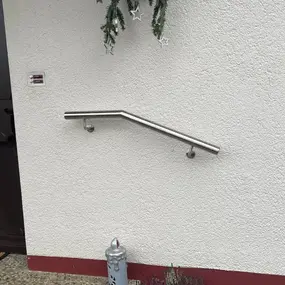 Edelstahl-Handlauf an weißer Hauswand neben Haustür, modernes Geländer für Eingang.