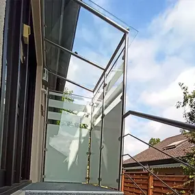 Modernes Balkongeländer aus Glas und Edelstahl an einem Haus mit Blick in den Garten.
