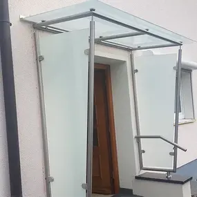 Modernes Vordach aus Glas mit Edelstahlsäulen an einem Hauseingang mit Treppe.