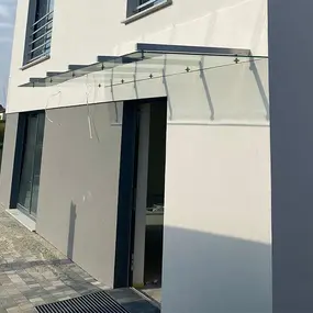 Modernes Glasvordach an einem Hauseingang mit stilvoller Fassade und gepflastertem Weg.