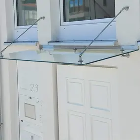 Modernes Glasvordach mit Edelstahlhalterungen über einer weißen Hauseingangstür montiert.