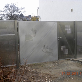 Moderner Sichtschutzzaun und Gartentor aus Edelstahl mit Lochmuster vor einem Haus.