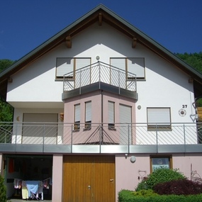 Modernes Einfamilienhaus mit Balkon und Garage, umgeben von Garten und blauer Himmel.