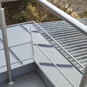 Edelstahlgeländer auf Flachdach mit moderner Dachabdichtung und Blick auf Wellblechdach.