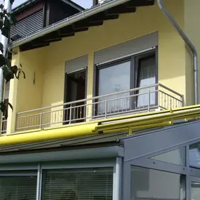 Gelbes Einfamilienhaus mit Balkon, Markise und modernem Wintergarten aus Glas.