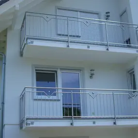 Zwei moderne Balkone mit Edelstahlgeländer an einer weißen Hausfassade.